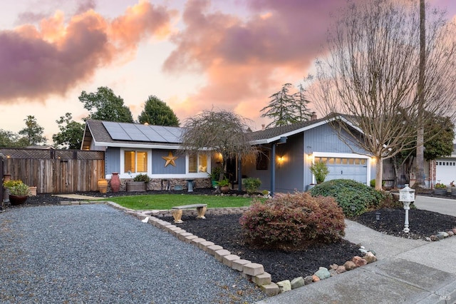 ranch-style house with a front yard, fence, an attached garage, and solar panels