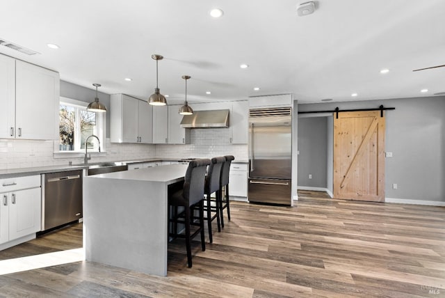 kitchen with wood finished floors, a sink, stainless steel appliances, a barn door, and wall chimney range hood