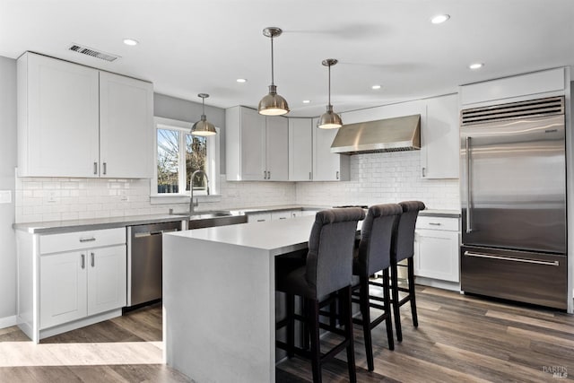 kitchen with visible vents, dark wood-type flooring, a sink, stainless steel appliances, and wall chimney range hood