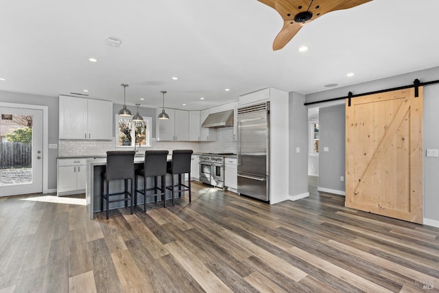 kitchen featuring plenty of natural light, a barn door, a kitchen breakfast bar, wall chimney exhaust hood, and premium appliances