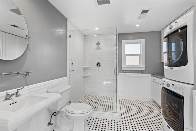 bathroom featuring visible vents, stacked washing maching and dryer, a sink, a shower stall, and wainscoting