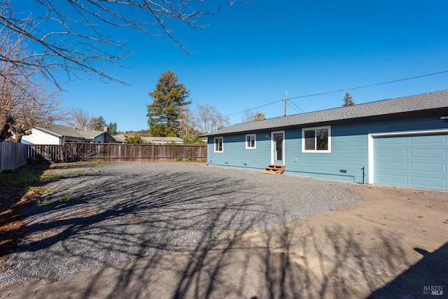 rear view of property featuring a garage, entry steps, driveway, and fence