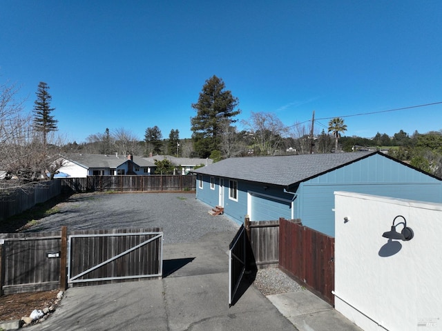 exterior space featuring a gate, fence, and roof with shingles