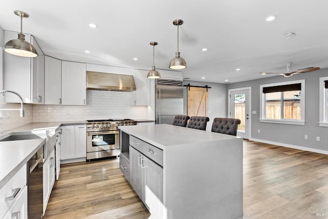 kitchen with a center island, high quality appliances, a barn door, wall chimney exhaust hood, and a sink