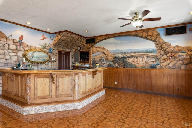 bar with a textured ceiling, ceiling fan, a dry bar, and crown molding