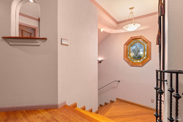 stairway featuring baseboards, wood finished floors, and crown molding