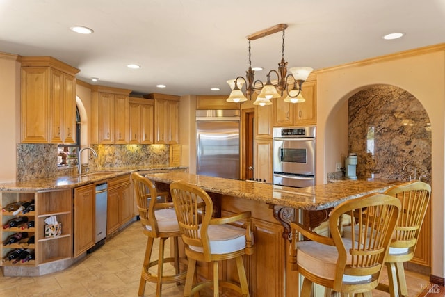 kitchen with arched walkways, a sink, appliances with stainless steel finishes, light stone countertops, and tasteful backsplash