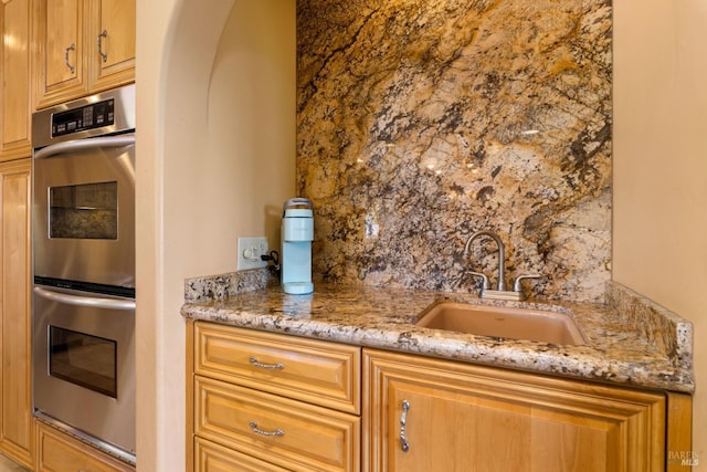 kitchen featuring stainless steel double oven, a sink, and light stone countertops