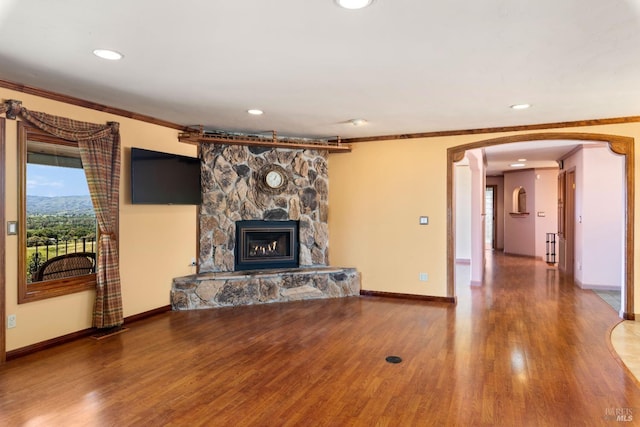 unfurnished living room featuring baseboards, arched walkways, ornamental molding, wood finished floors, and a stone fireplace