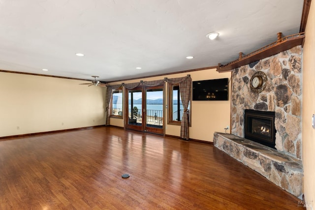 unfurnished living room with crown molding, baseboards, wood finished floors, and a stone fireplace