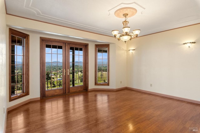 empty room featuring a wealth of natural light, a chandelier, wood finished floors, and french doors