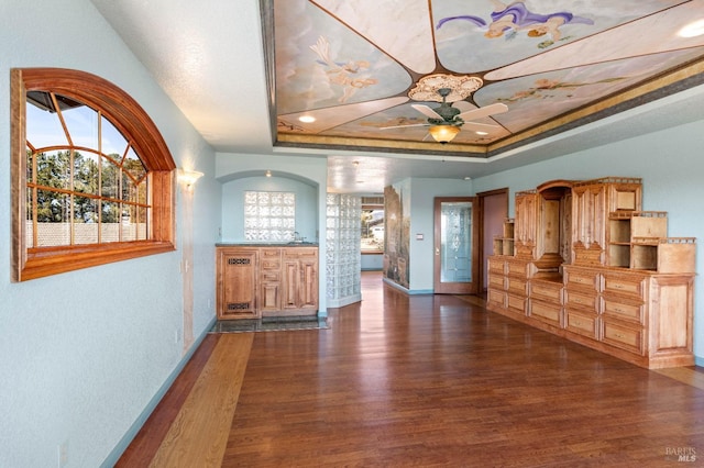 living area with ceiling fan, dark wood-type flooring, a raised ceiling, and baseboards