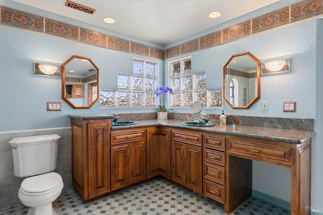 bathroom featuring tile walls, visible vents, a textured wall, toilet, and vanity