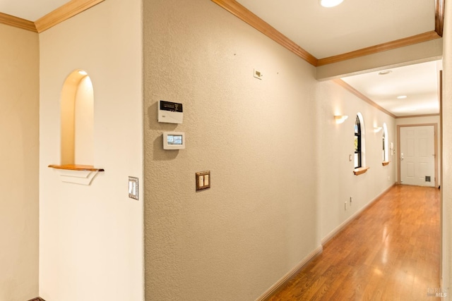 hallway featuring light wood-style floors, a textured wall, crown molding, and baseboards