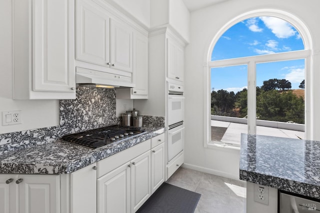 kitchen with double oven, white cabinetry, custom range hood, backsplash, and stainless steel gas stovetop