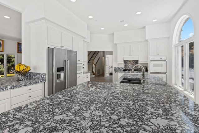 kitchen featuring dark stone countertops, high end refrigerator, white cabinets, and a sink