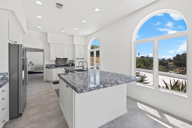 kitchen featuring a center island with sink, visible vents, white cabinetry, a sink, and stainless steel fridge