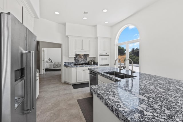 kitchen with high end refrigerator, white cabinetry, a sink, and oven