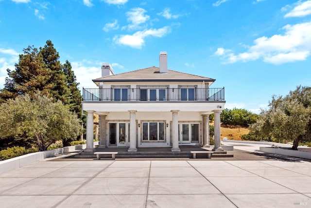 back of house featuring a balcony, a chimney, and stucco siding