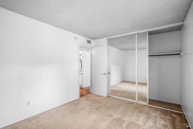 unfurnished bedroom featuring carpet, a textured ceiling, visible vents, and a closet