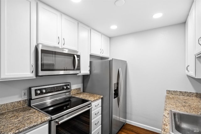 kitchen with dark wood-style flooring, stainless steel appliances, white cabinets, a sink, and baseboards