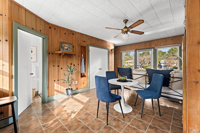 dining room featuring wood walls, a ceiling fan, and tile patterned floors