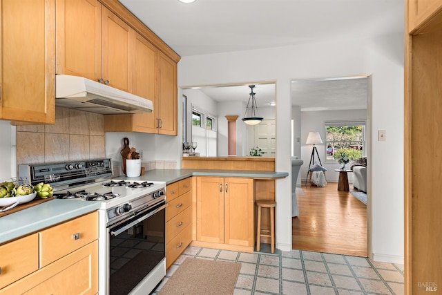 kitchen with white range with gas stovetop, light floors, a peninsula, under cabinet range hood, and backsplash