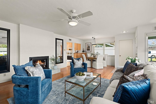 living area featuring ceiling fan, a lit fireplace, wood finished floors, and baseboards