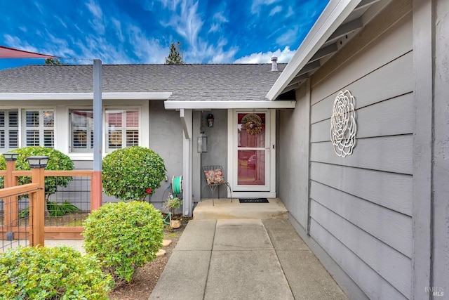 property entrance with a shingled roof, fence, and stucco siding