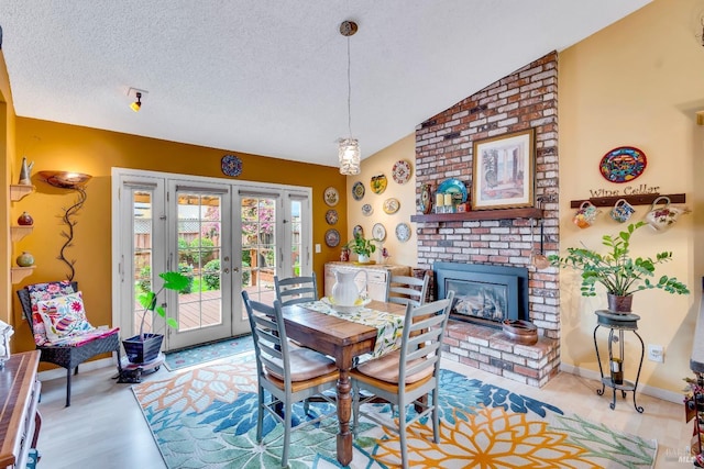 dining space with baseboards, vaulted ceiling, a textured ceiling, french doors, and a fireplace