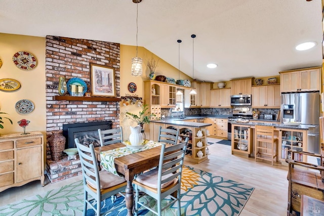 dining room featuring vaulted ceiling, recessed lighting, a fireplace, and light wood-style floors