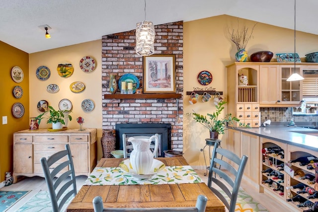 dining area featuring a brick fireplace, vaulted ceiling, and light wood finished floors