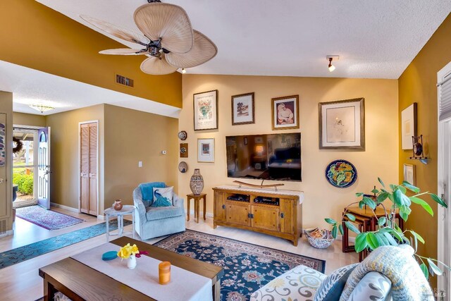 living area featuring visible vents, vaulted ceiling, a textured ceiling, ceiling fan, and baseboards