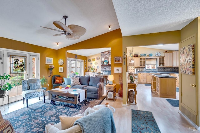 living area featuring vaulted ceiling, a textured ceiling, light wood-type flooring, and a ceiling fan