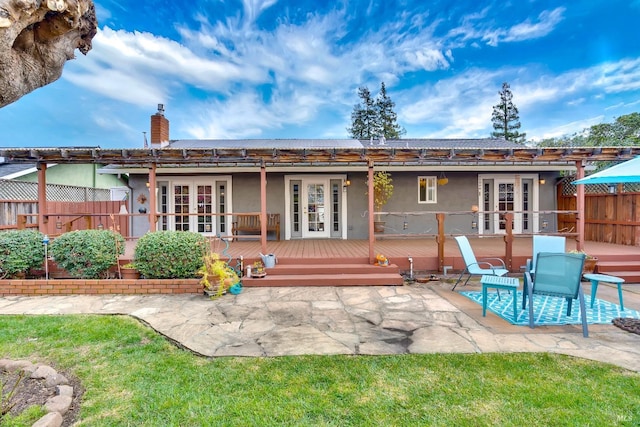 rear view of property featuring french doors, a chimney, fence, a wooden deck, and stucco siding