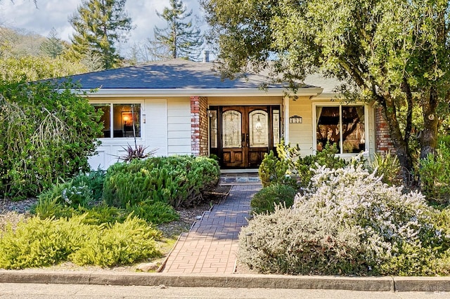 single story home featuring french doors, a shingled roof, and brick siding