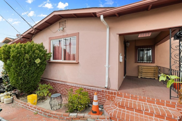 view of exterior entry with brick siding, a patio area, and stucco siding