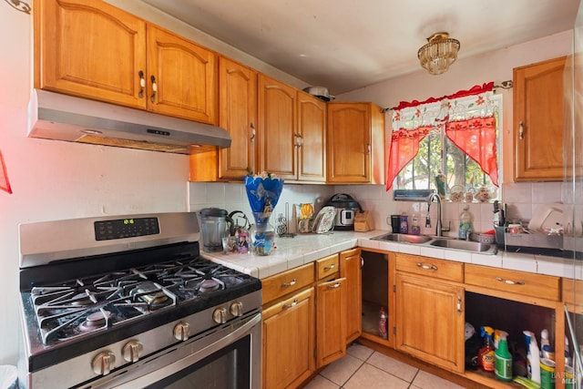 kitchen with light tile patterned floors, tile counters, under cabinet range hood, a sink, and gas stove