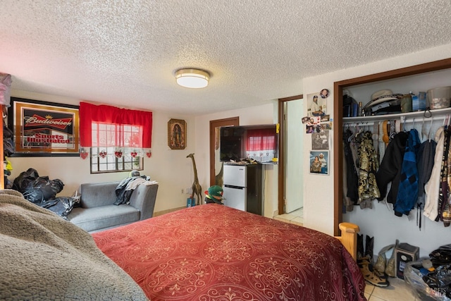 tiled bedroom with freestanding refrigerator, a closet, and a textured ceiling