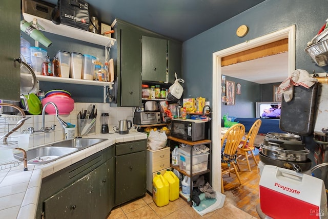 kitchen featuring tile countertops, black microwave, light tile patterned flooring, a sink, and backsplash