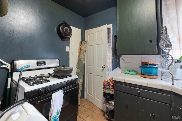 kitchen featuring range with gas cooktop, light tile patterned floors, tile counters, decorative backsplash, and dark cabinetry