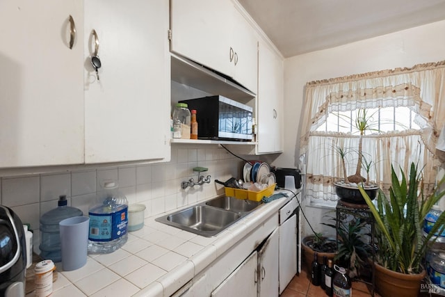 kitchen featuring stainless steel microwave, a sink, tile counters, and white cabinets