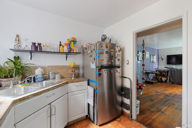 kitchen with light tile patterned flooring, a sink, light countertops, freestanding refrigerator, and open shelves