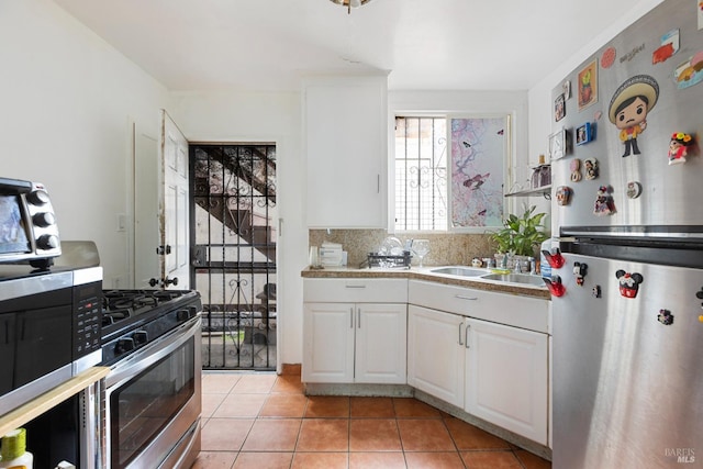 kitchen with light tile patterned floors, decorative backsplash, stainless steel appliances, white cabinetry, and a sink