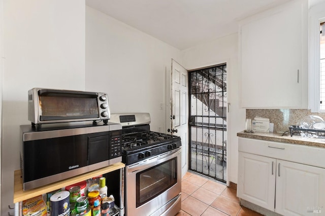 kitchen featuring light tile patterned floors, white cabinets, decorative backsplash, stainless steel appliances, and light countertops