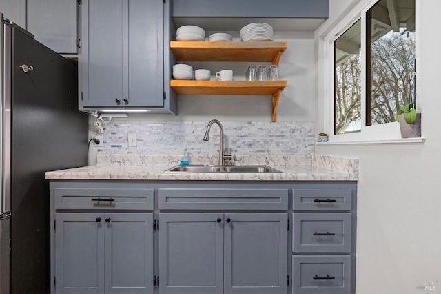 kitchen with tasteful backsplash, gray cabinets, a sink, and freestanding refrigerator