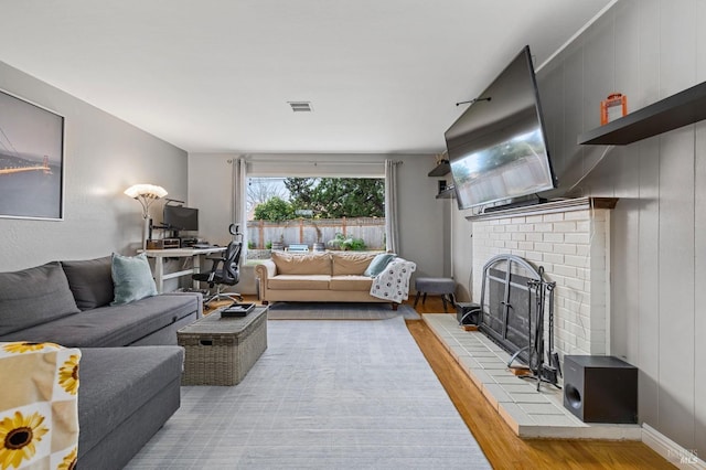 living room featuring light wood-type flooring, a brick fireplace, and visible vents