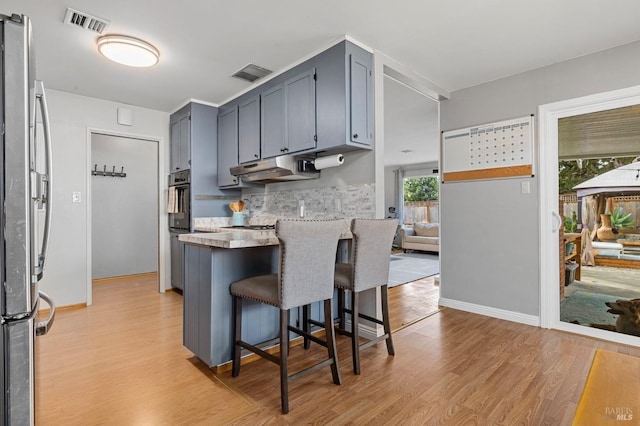 kitchen featuring freestanding refrigerator, a peninsula, gray cabinetry, light wood-type flooring, and under cabinet range hood