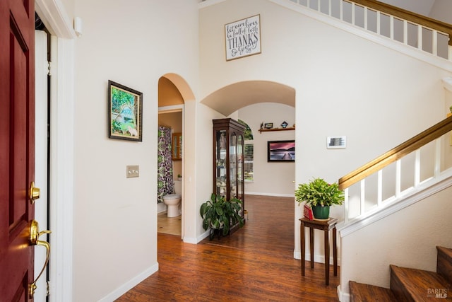 entrance foyer featuring arched walkways, wood finished floors, a towering ceiling, baseboards, and stairs