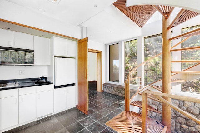 kitchen featuring cooktop, white cabinets, dark countertops, white fridge, and black microwave